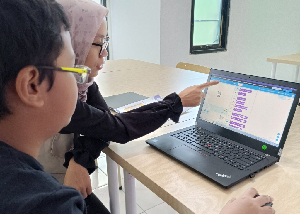 Guru sedang mengajarkan coding kepada anak didiknya